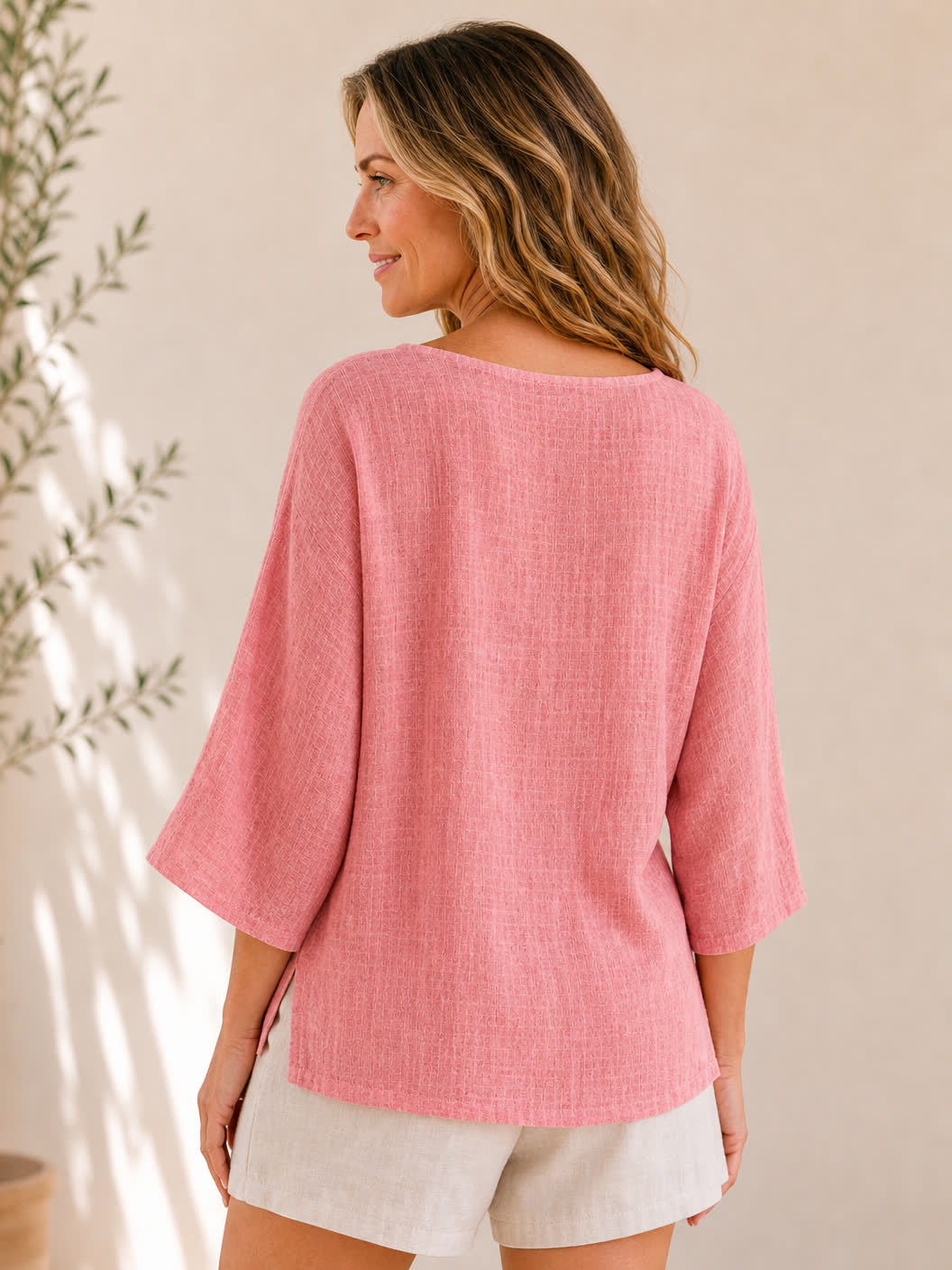 Back view of a woman wearing a pink LoomBasics crew neck 100% cotton blouse and beige shorts.