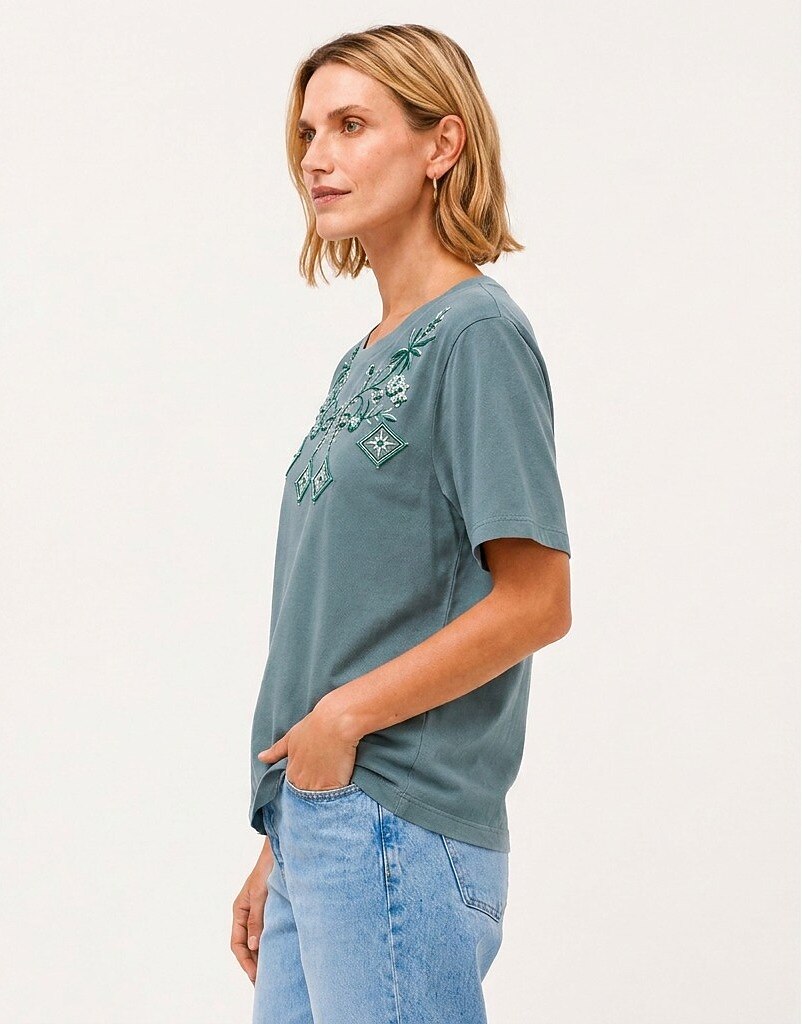 Woman wearing a LoomBasics Geometric Tropical Cotton Tee in muted blue with green embroidery.