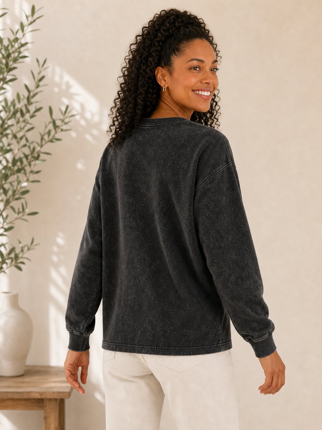 Woman wearing a LoomBasics grey acid wash 100% cotton crewneck sweatshirt and white pants.