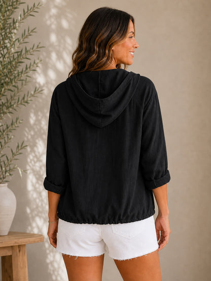 Woman wearing a black LoomBasics 100% cotton hooded drawstring shirt and white denim shorts.