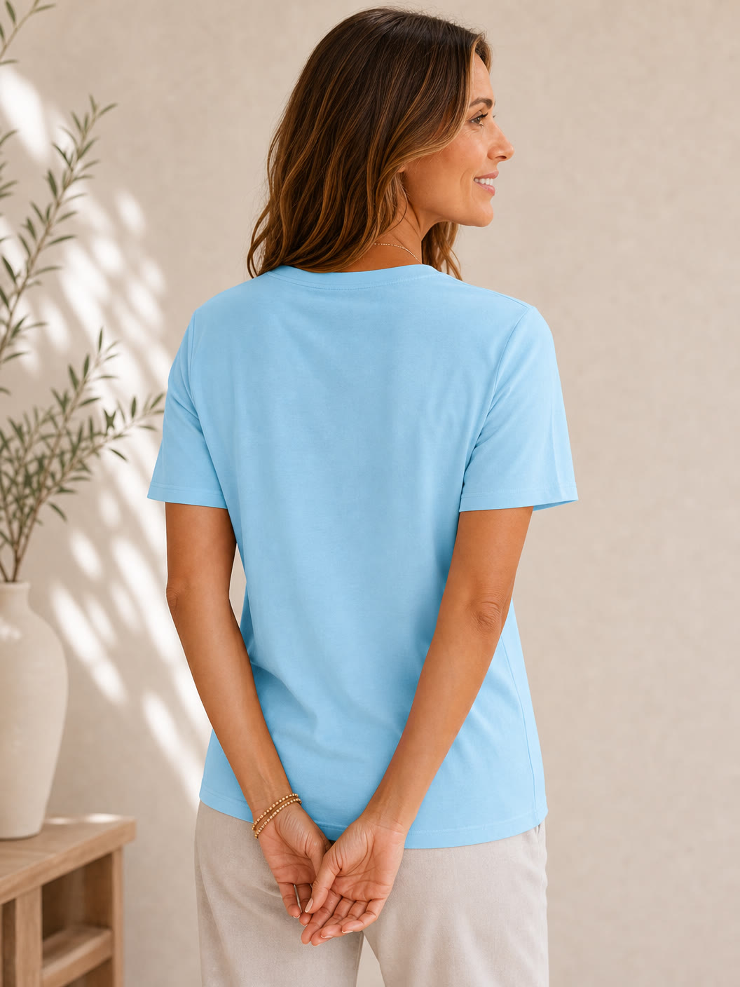 Back view of a woman wearing a LoomBasics light blue 100% cotton v neck tee and beige pants