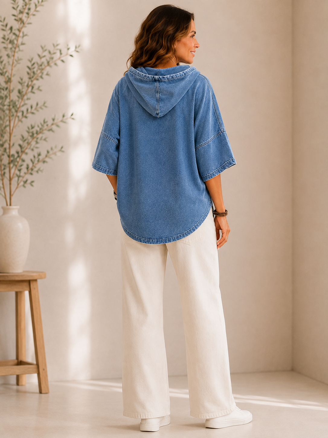 Woman from behind wearing a LoomBasics washed blue cotton hooded sweatshirt and white wide-leg pants.