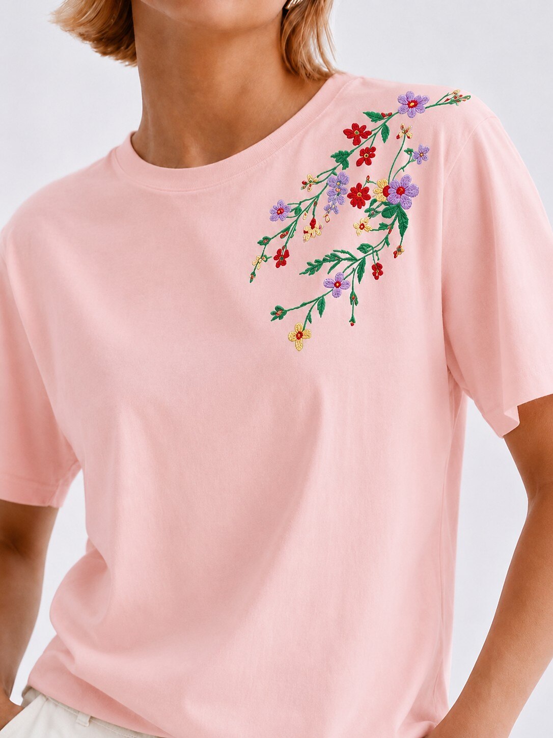 Woman wearing a LoomBasics light pink 100% cotton tee with colorful floral embroidery on the shoulder