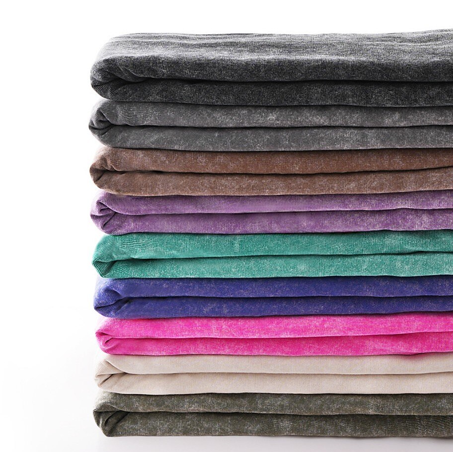 Stack of colorful LoomBasics 100% cotton crew neck tees in various muted and vibrant tones.