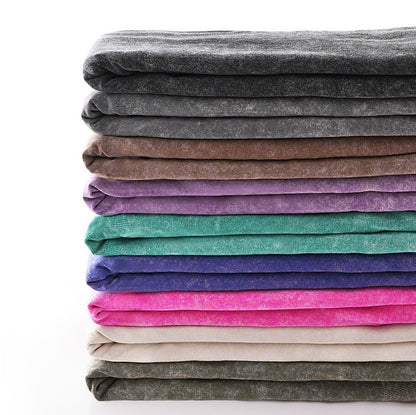 Stack of colorful LoomBasics 100% cotton crew neck tees in various muted and vibrant tones.