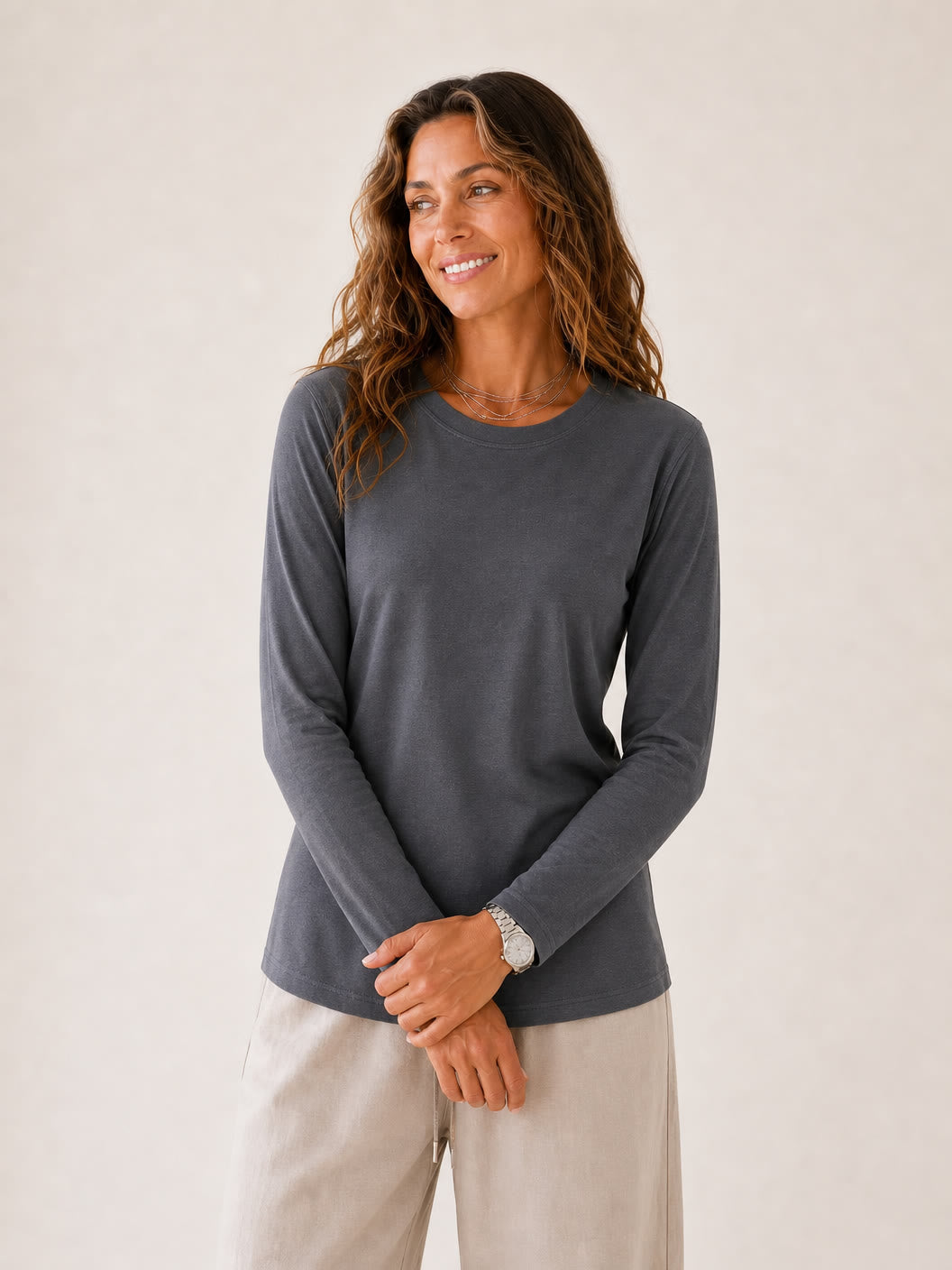 Woman wearing a charcoal grey 100% cotton crew neck long sleeve tee and beige trousers.