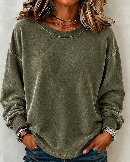 Woman wearing a LoomBasics washed olive green 100% cotton crewneck sweatshirt and blue jeans.