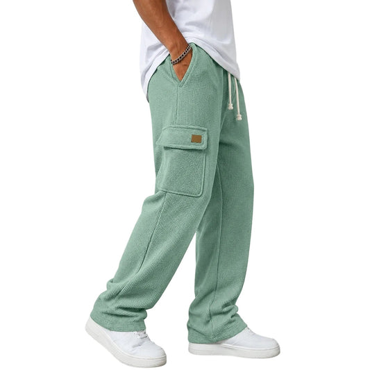 A person wearing light sage green textured cargo sweatpants with white sneakers, standing against a white wall.