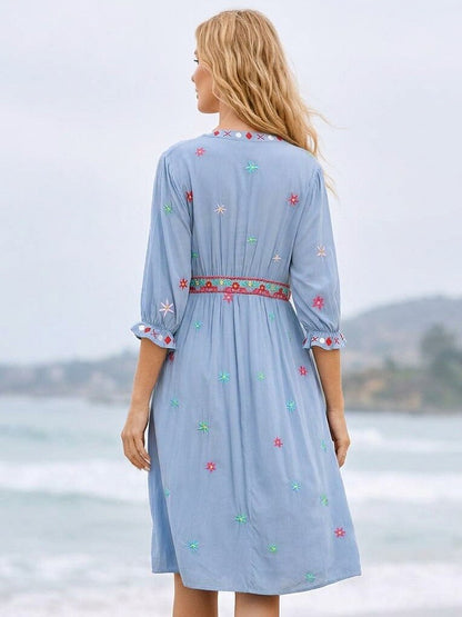 Back view of a woman wearing a light blue LoomBasics embroidered cotton mini dress on a beach.