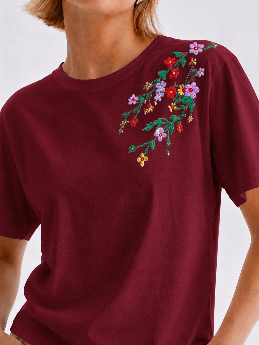 Woman wearing a maroon LoomBasics cotton tee with colorful floral embroidery on the shoulder