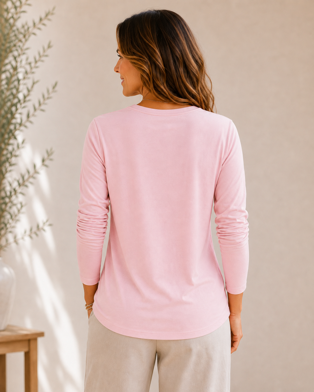 Back view of a woman wearing a LoomBasics pink 100% cotton long sleeve crew neck tee.