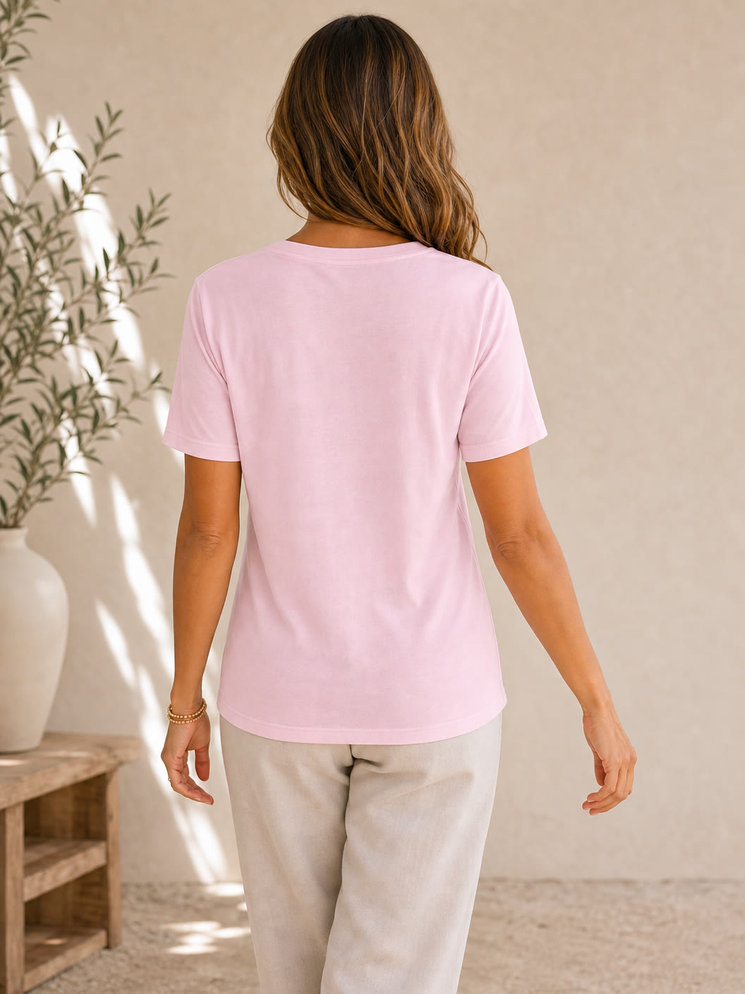 Back view of a woman wearing a light pink LoomBasics 100% cotton v-neck tee and beige pants.