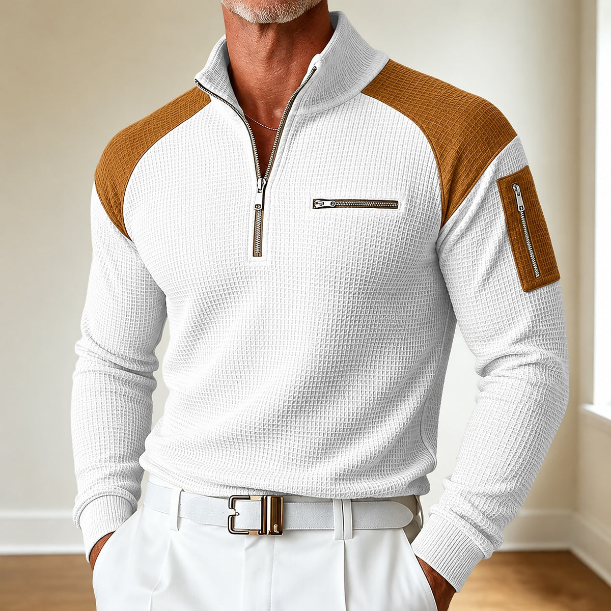 A man wearing a white waffle-knit quarter-zip pullover sweater with brown color-blocked shoulder panels and a matching brown sleeve patch, paired with white trousers and a white belt.