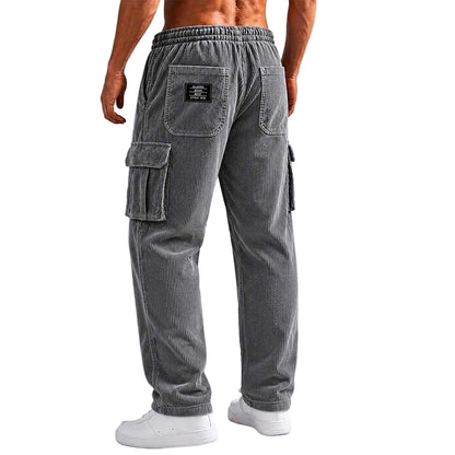 A man wearing gray corduroy cargo pants, shown from the back. The pants feature an elastic waistband, two back cargo pockets, and side cargo pockets, paired with white sneakers