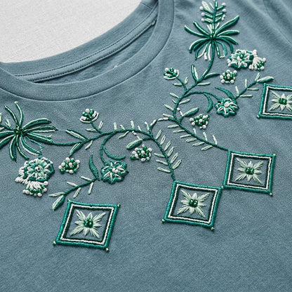 Close-up of green floral and geometric embroidery on a LoomBasics blue cotton tee.