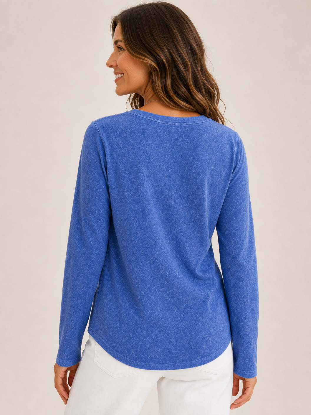 Back view of a woman wearing a LoomBasics washed blue cotton long sleeve v-neck top and white pants.