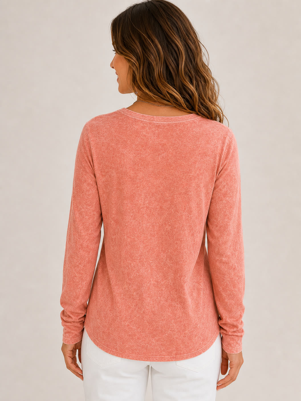 Back view of a woman wearing a LoomBasics washed cotton long sleeve top in coral pink.