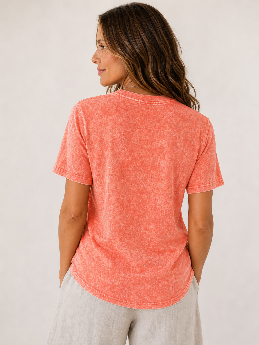 Back view of a woman wearing a LoomBasics coral acid wash 100% cotton crew neck tee.