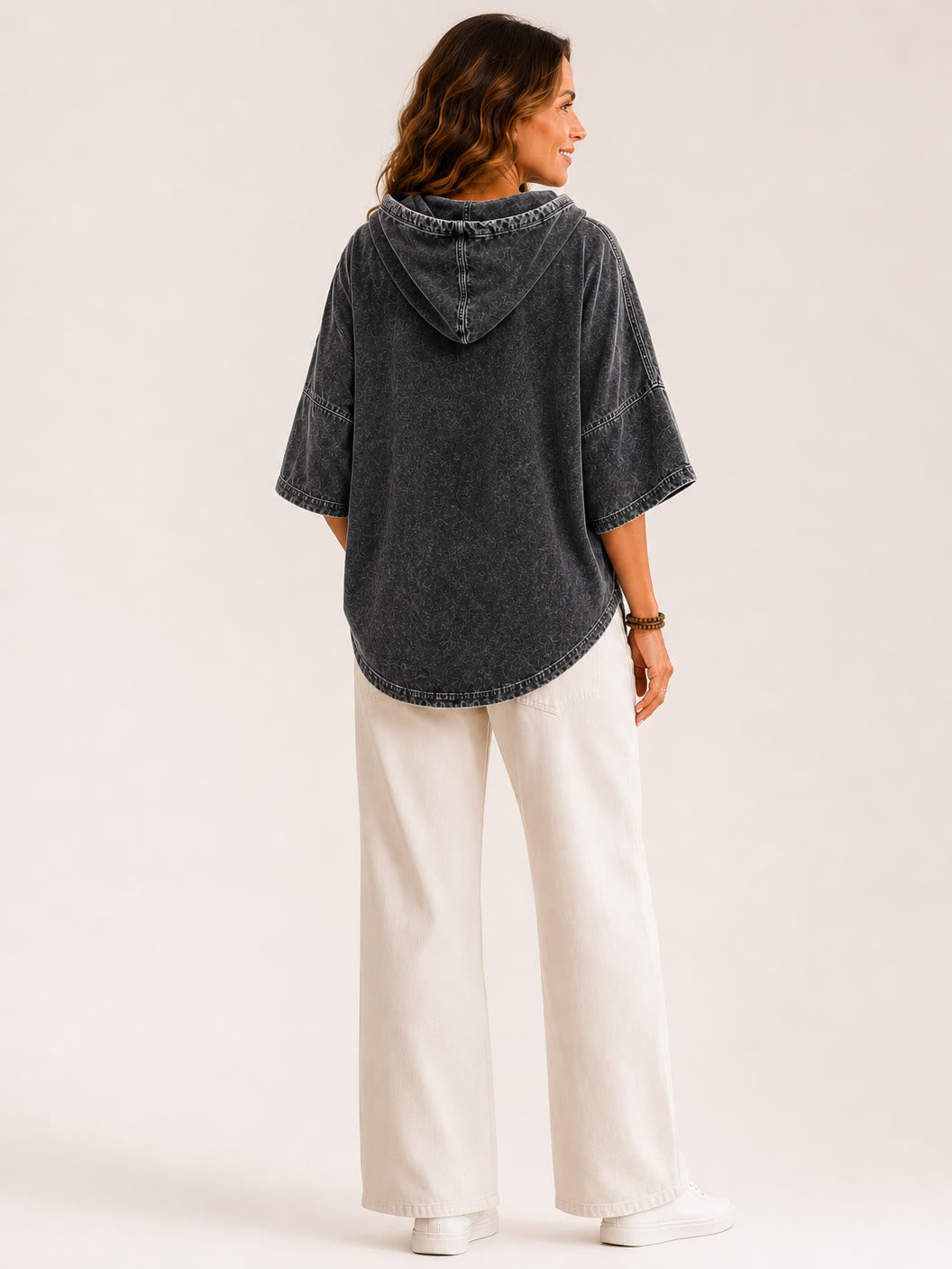 Back view of a woman wearing a LoomBasics washed cotton hooded sweatshirt and white wide-leg pants.
