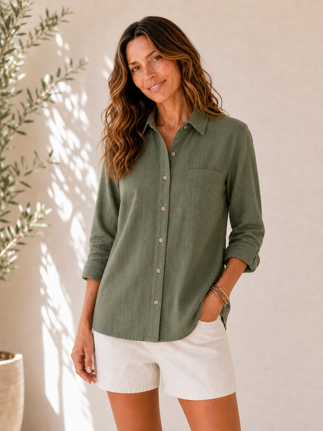 Woman wearing a LoomBasics olive green 100% cotton pocket button-up shirt and white shorts.