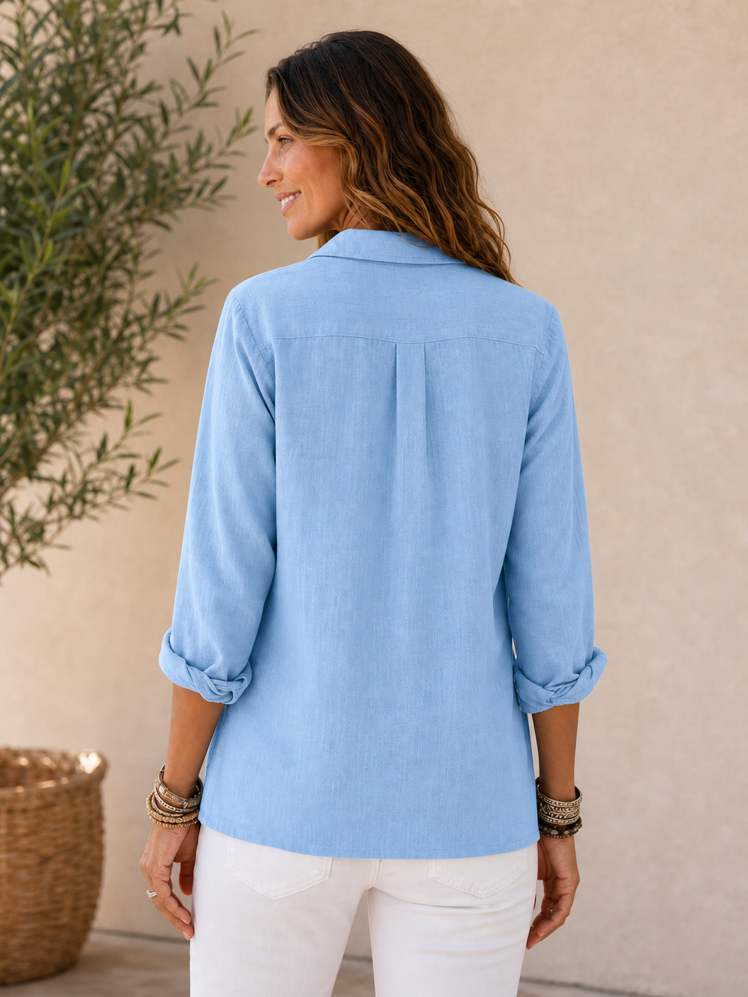 Back view of a woman wearing a light blue LoomBasics 100% cotton button-up shirt and white pants.