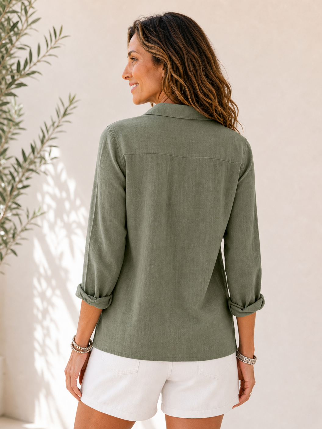Back view of a woman wearing a LoomBasics olive green cotton button-up shirt and white shorts.