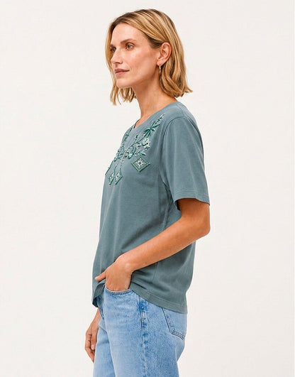 Woman wearing a LoomBasics Geometric Tropical Cotton Tee in muted blue with green embroidery.