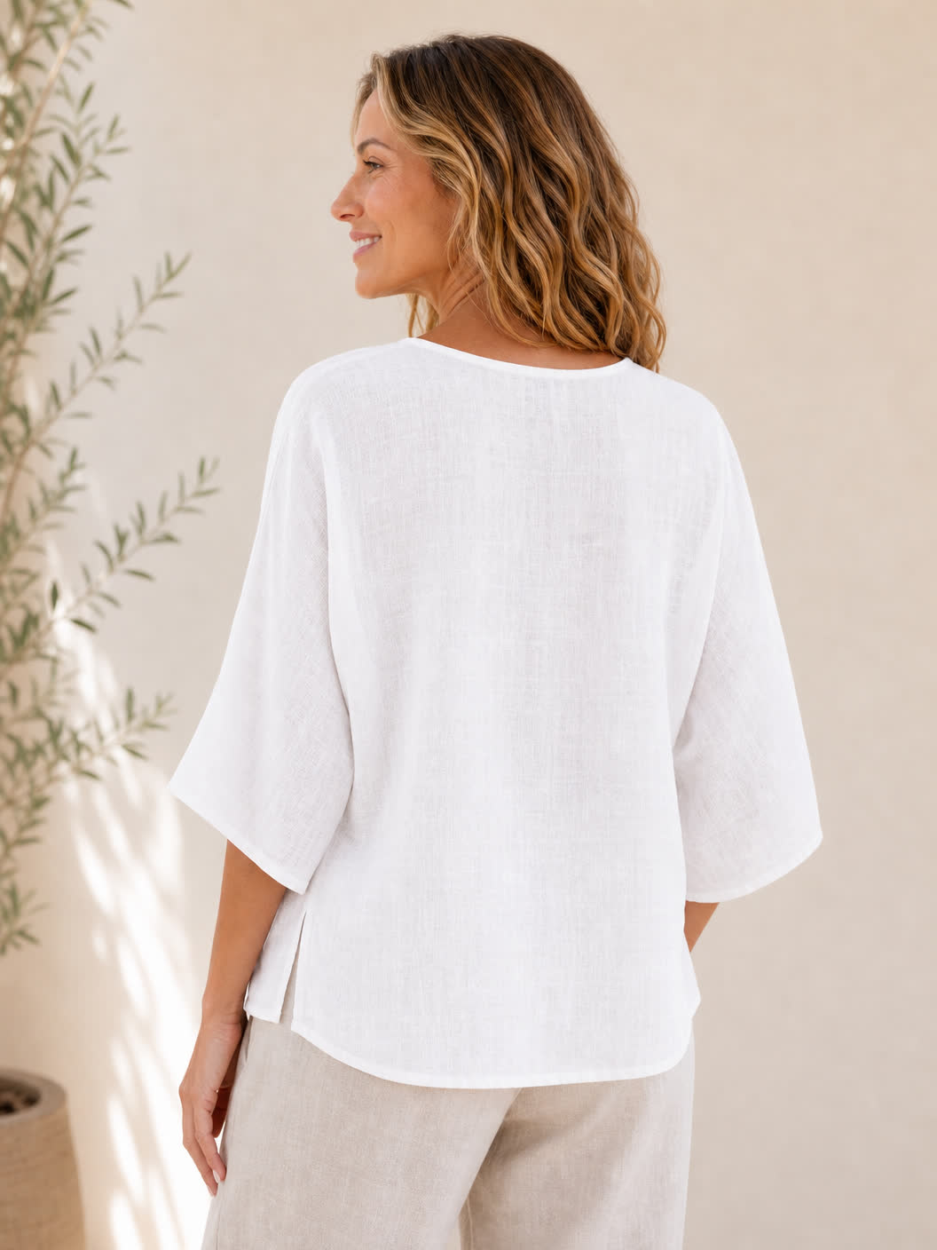 Back view of a woman wearing a LoomBasics white crew neck 100% cotton blouse and beige pants.