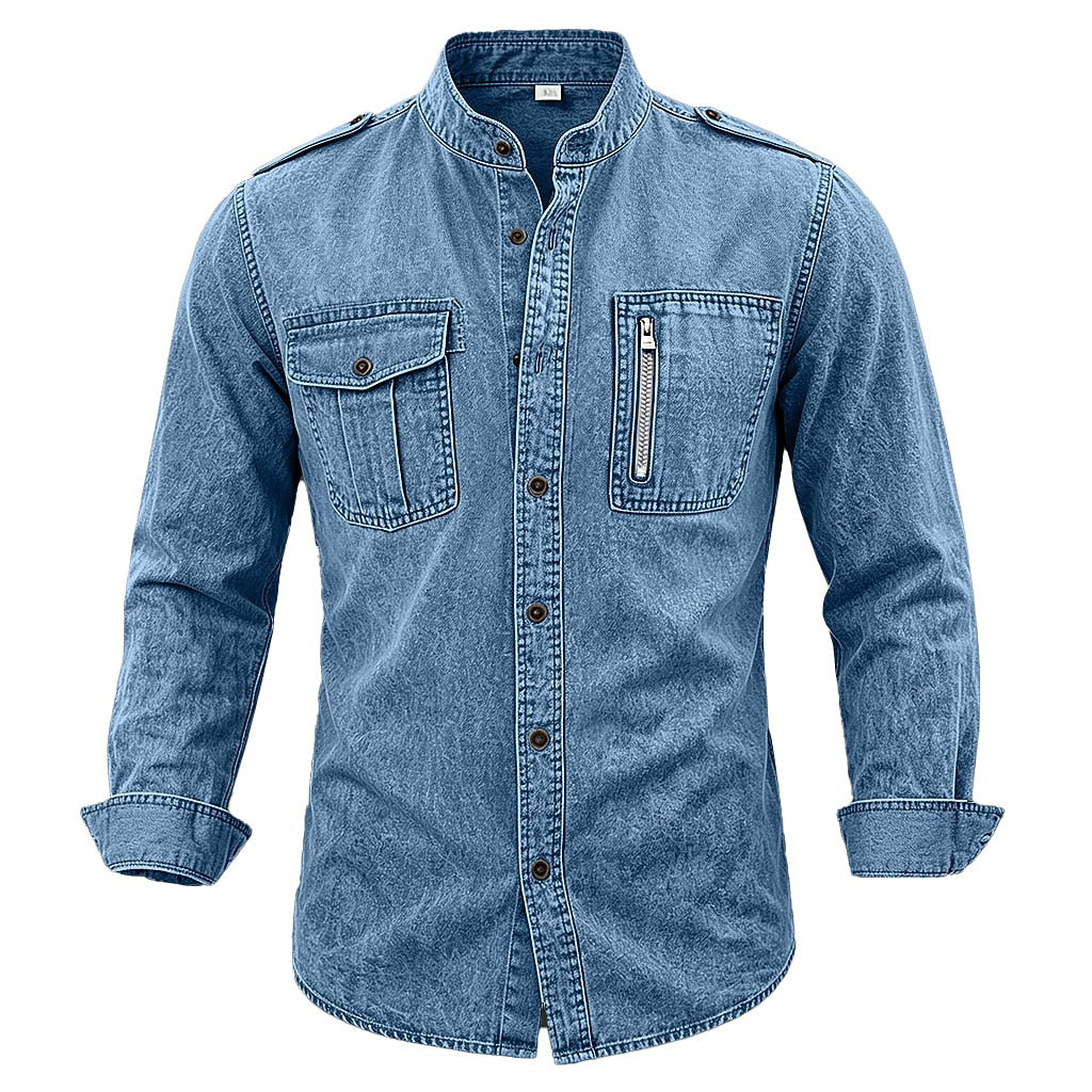 A men's long-sleeve denim shirt jacket in a medium blue wash, featuring a stand collar, button-down front, two flap chest pockets, and a zippered chest pocket, shown on a plain white background.