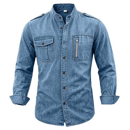 A men's long-sleeve denim shirt jacket in a medium blue wash, featuring a stand collar, button-down front, two flap chest pockets, and a zippered chest pocket, shown on a plain white background.