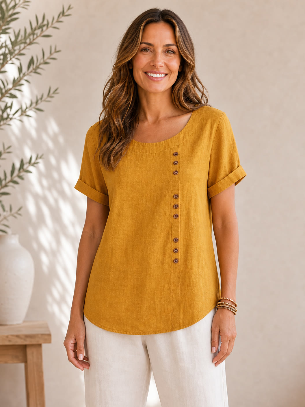 Woman wearing a mustard yellow LoomBasics soft button 100% cotton blouse and white pants.