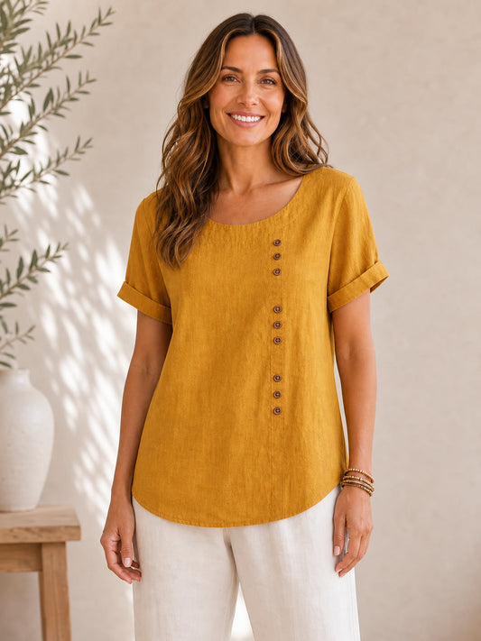 Woman wearing a mustard yellow LoomBasics soft button 100% cotton blouse and white pants.