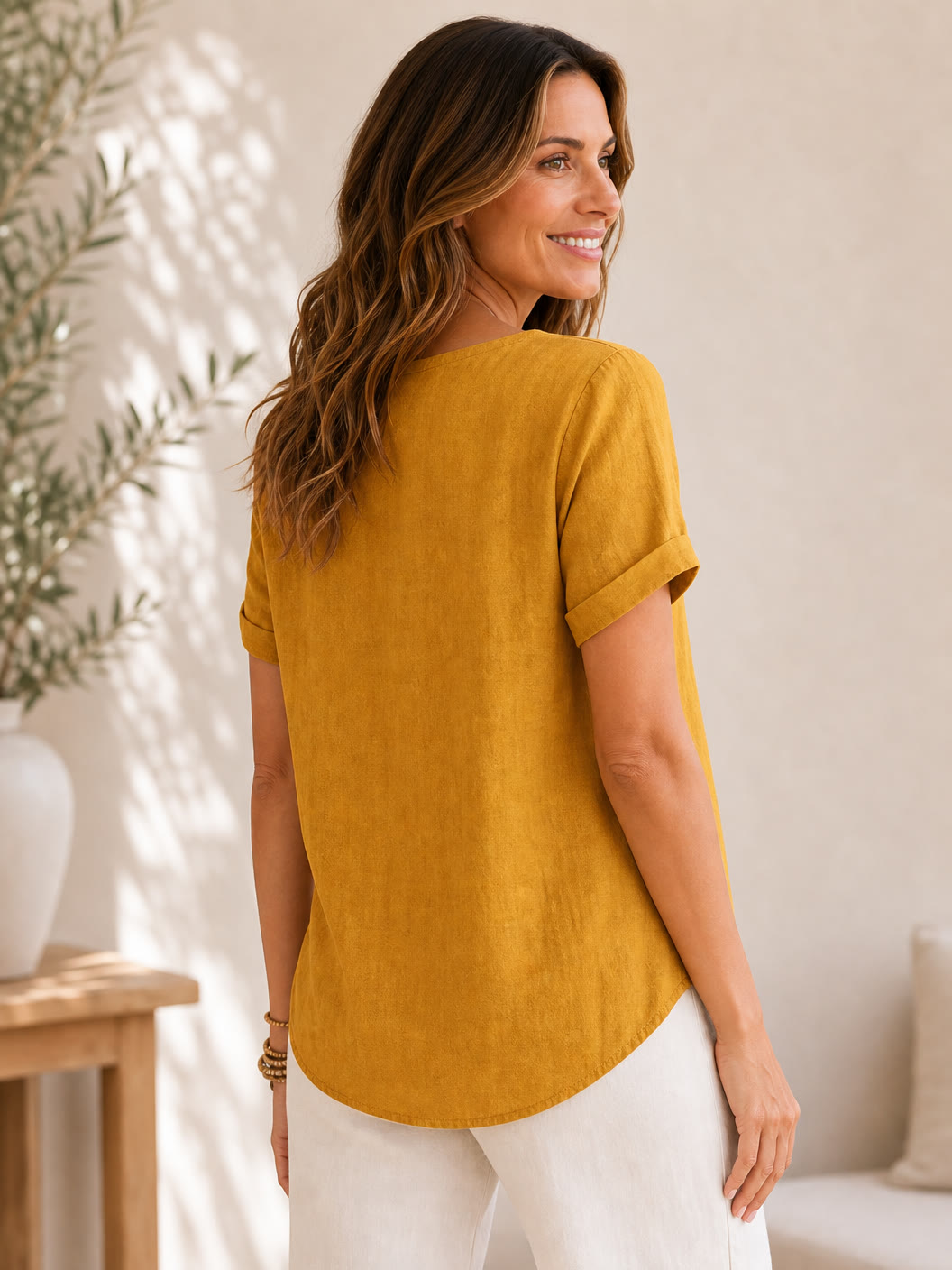 Woman wearing a LoomBasics mustard yellow 100% cotton short sleeve blouse and white pants.